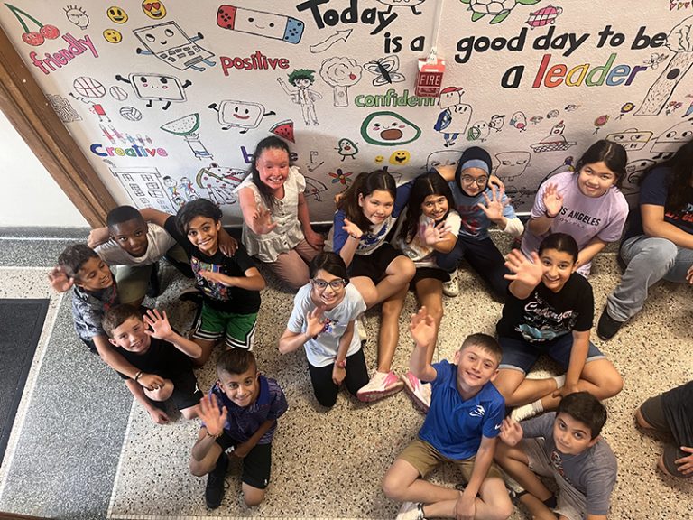 A group of students by a mural they are creating as part of the 2024 Summer Discovery Program at Lindbergh Elementary.